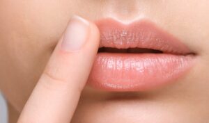 Woman with cold sore touching lips on light background